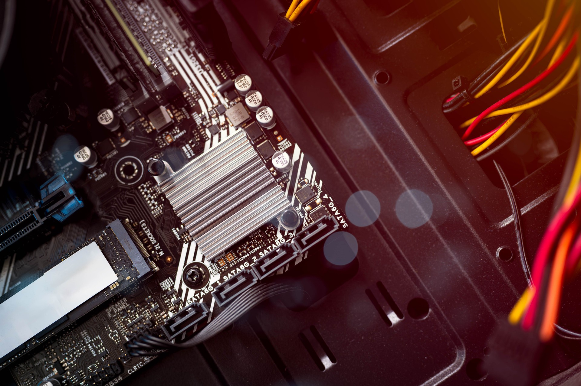 Closeup of computer motherboard with heatsink, SATA ports, and SSD slot inside desktop PC. Concept of hardware components, PC building, tech repair, and data transfer systems.